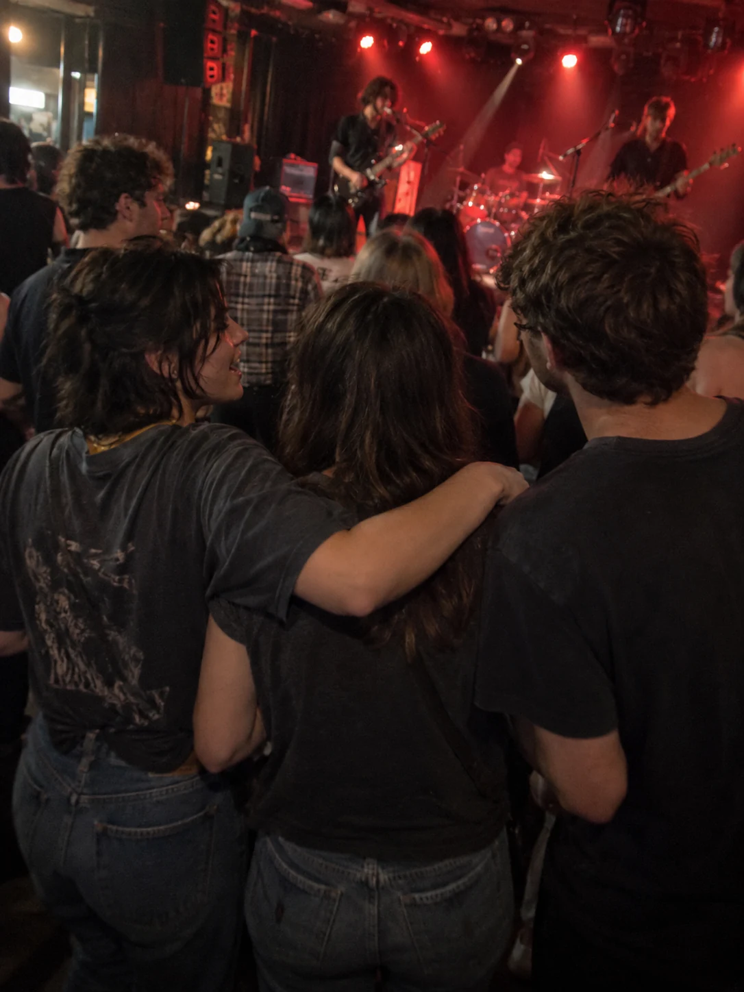 Un grupo de amigos abrazados entre el público, mirando una banda en vivo